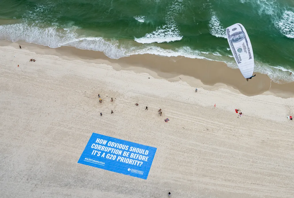 Paragliders with canopies depicting US$100 bills over a beach, about to touch down on a banner which read: “How obvious should corruption be before it’s a G20 priority?”