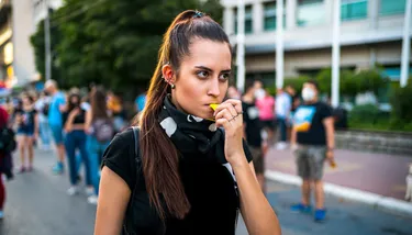 Woman activist walking down the street and blowing a whistle, with people in the background wearing medical masks