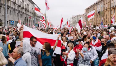 A large crowd protesting in the street waves red and white flags, some wear masks