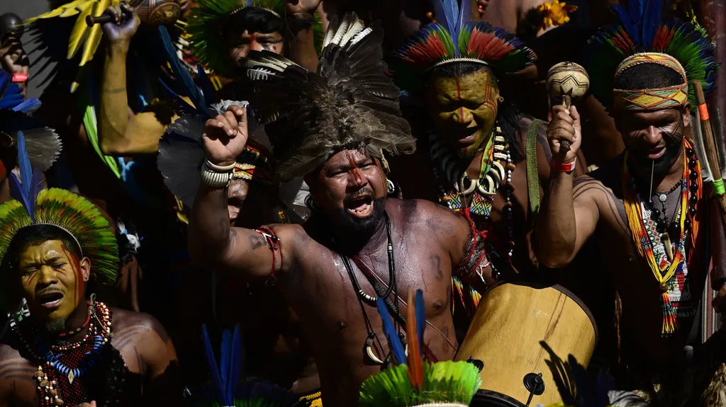 Indigenous people, wearing traditional attire, chanting and playing musical instruments during a demonstration to defend cultural rights in Brasilia, Brazil