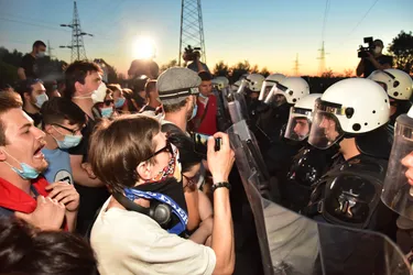 Protesters clash against police's shield at sunset. The police wear helmets and black suits, the protestors are in t shirt and most wear chirurgical masks