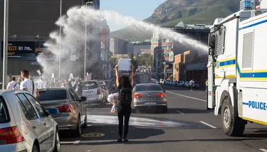 A police truck sprays a water jet over ta protester who holds a sign high